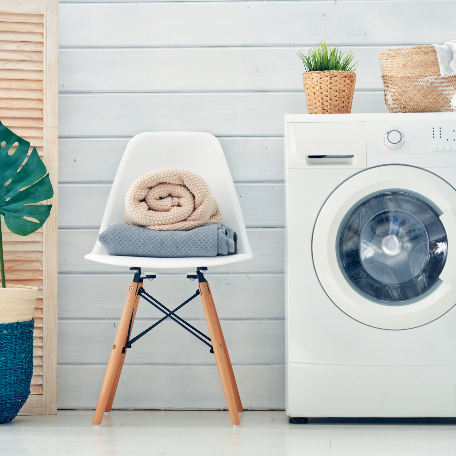 mid century modern chair with towels rolled on top between a washing machine and a monstera plant