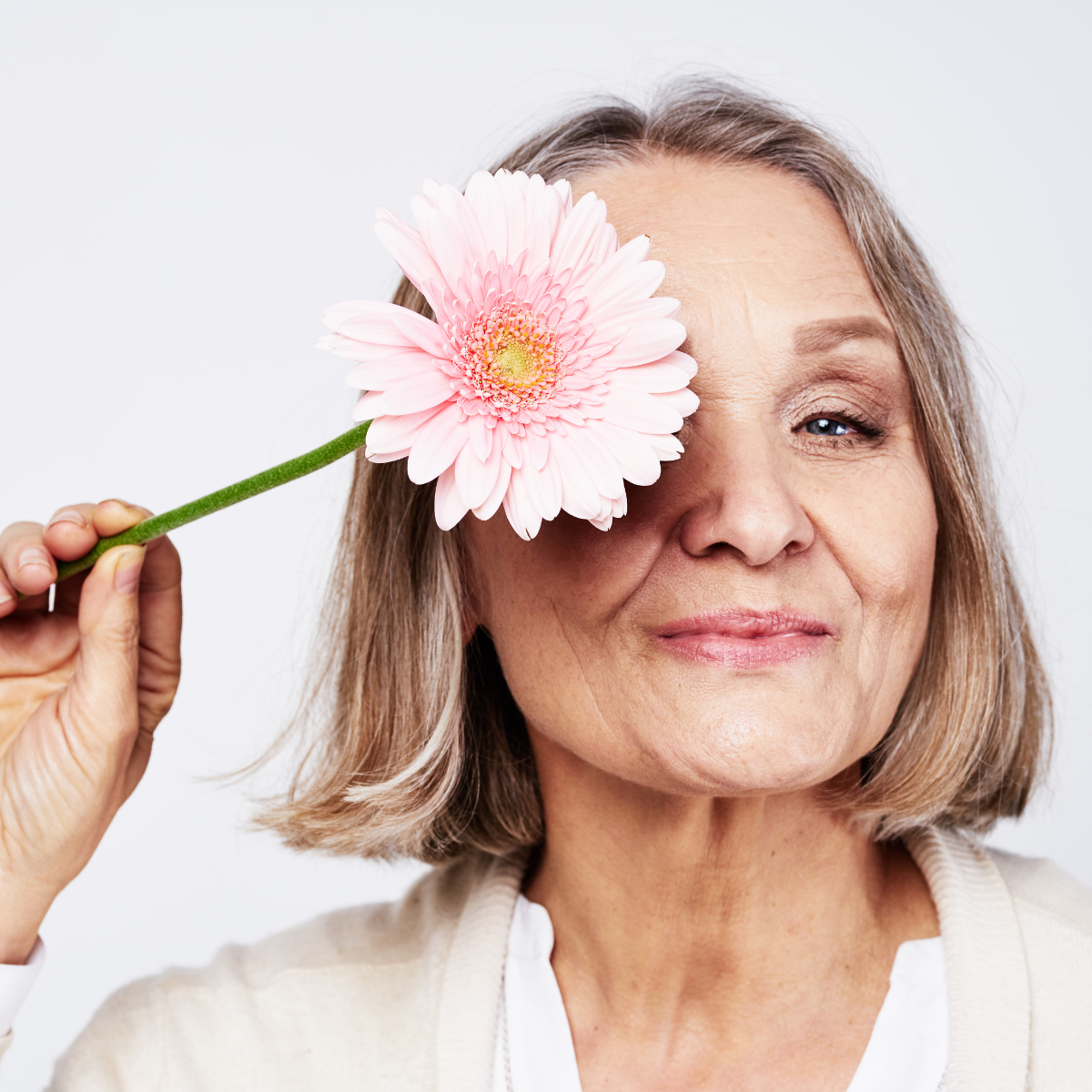 older women smiling in a sassy way with a light pink flower over one eye