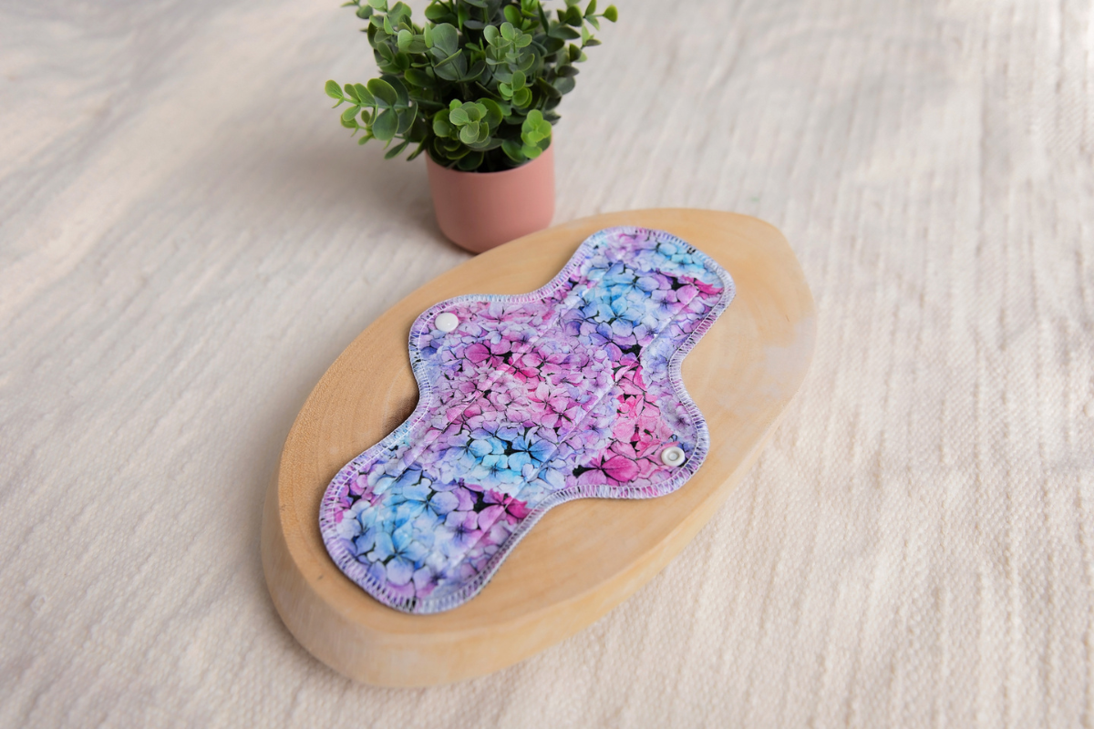 floral print reusable pad on white wooden oval beside green plant