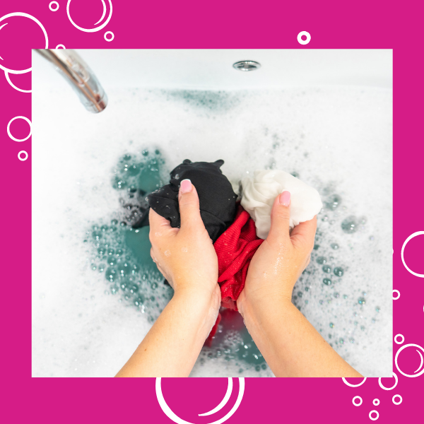 hands washing clothing in soapy water under faucet on hot pink background