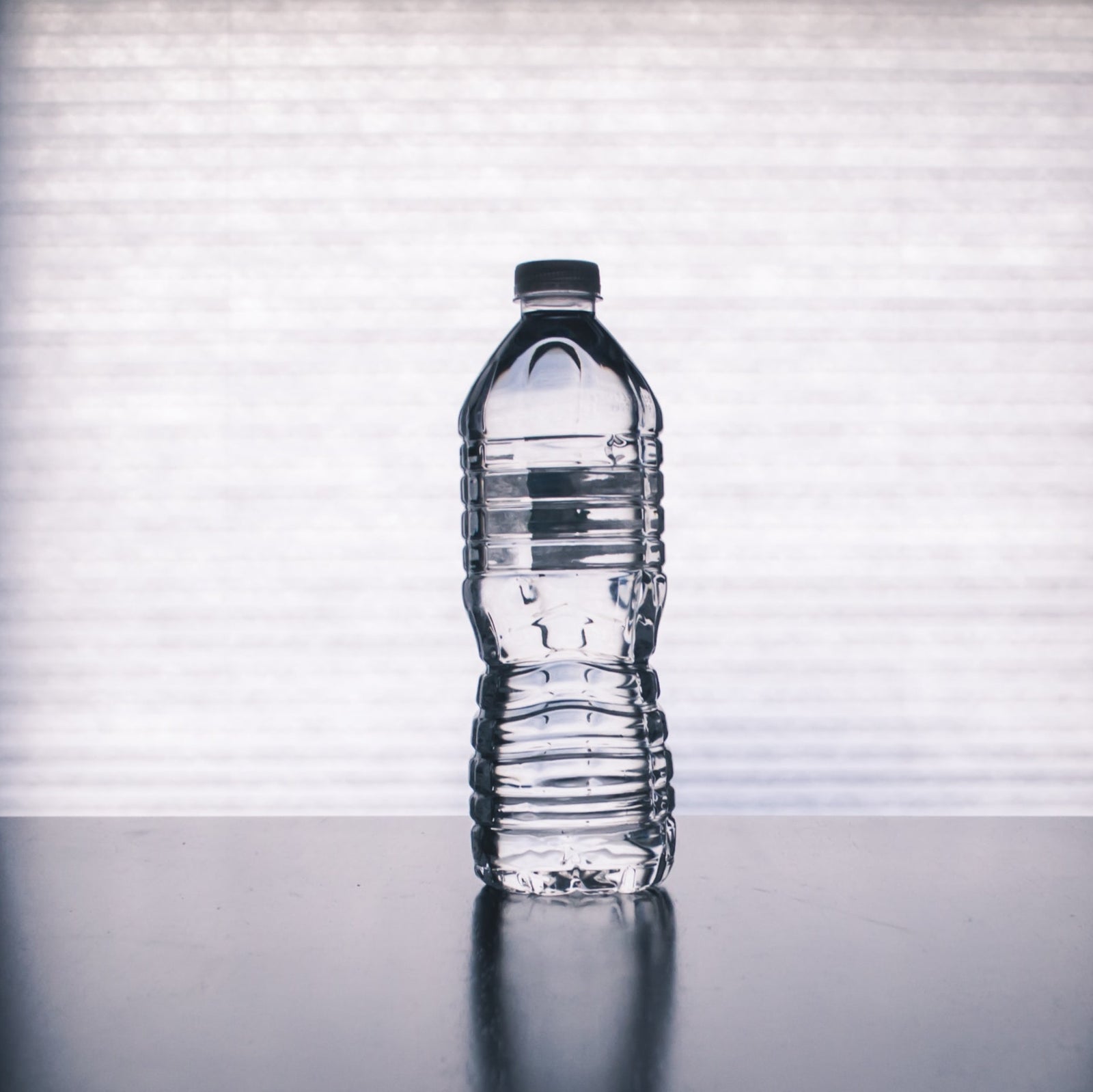 plastic water bottle sitting on glossy table casting reflection