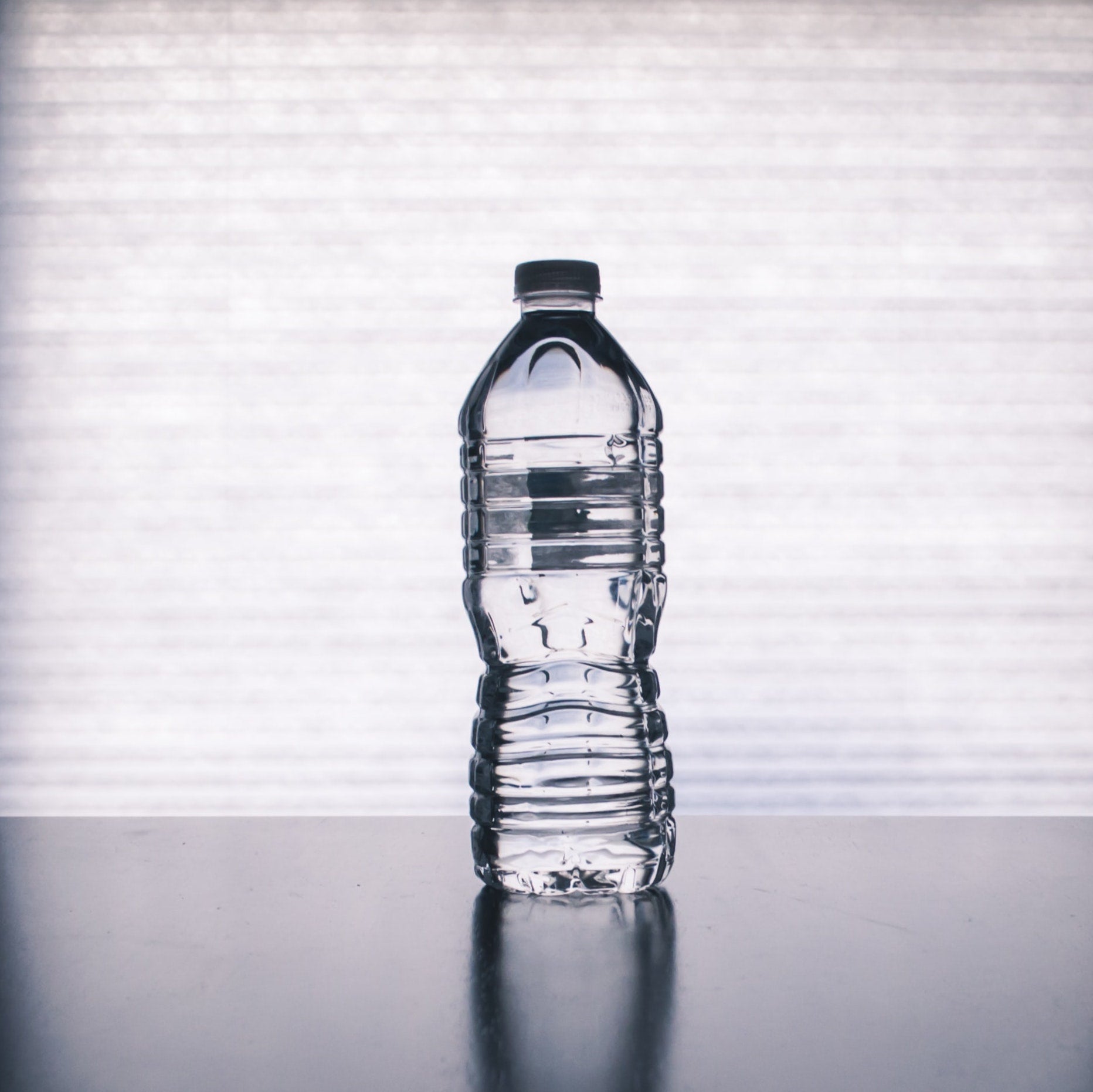 plastic water bottle sitting on glossy table casting reflection