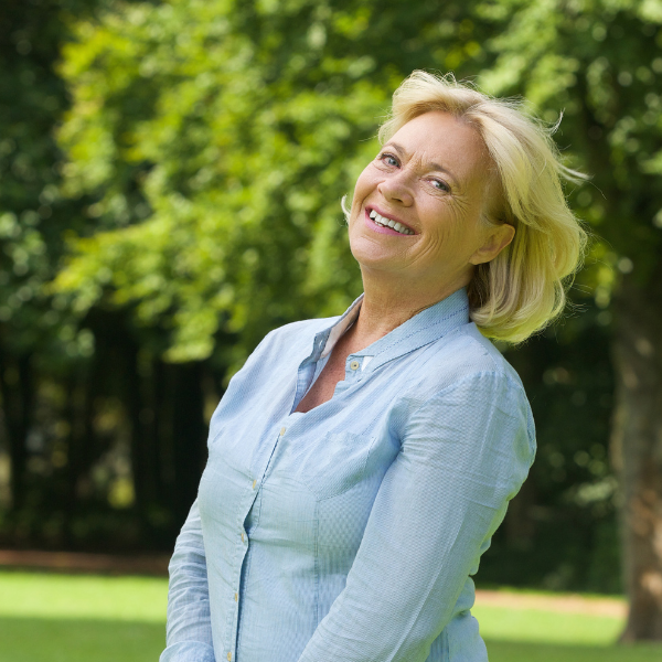 middle aged woman blonde hair blue button down shirt smiling outside trees reusable pads for incontinence