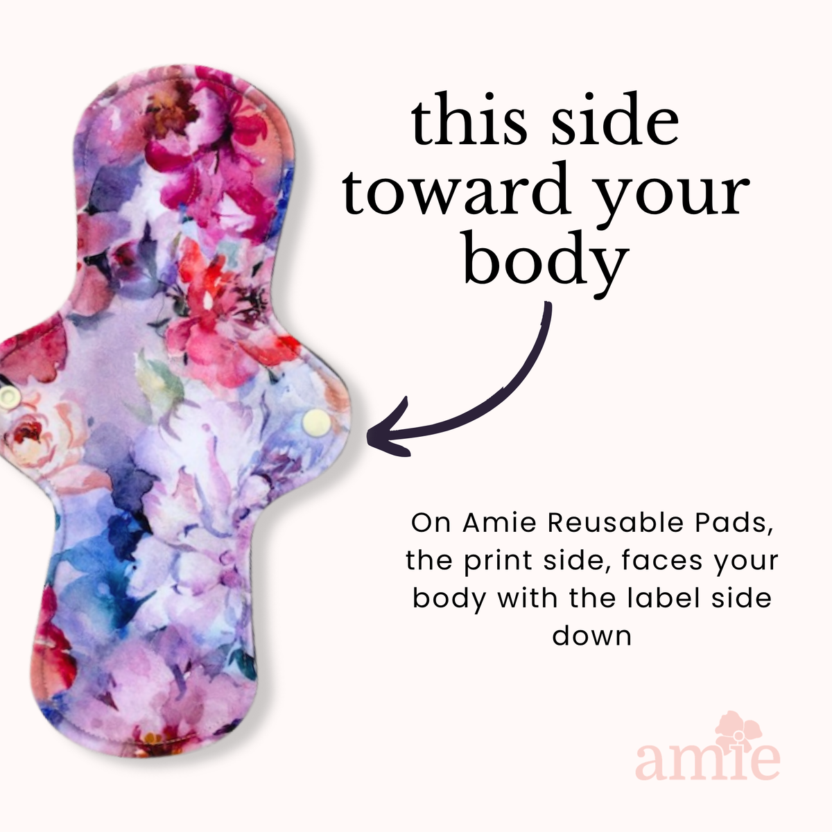 A reusable sanitary pad with a colourful floral watercolour print is shown on a light peach background with instructional text and an arrow indicating the correct orientation.