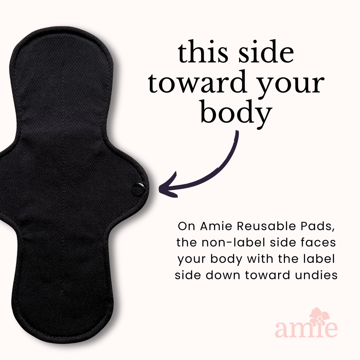 A black reusable menstrual pad shown on a light cream background with instructional text reading 'this side toward your body' and a small arrow pointing to the product. The Amie logo appears in the lower right corner.