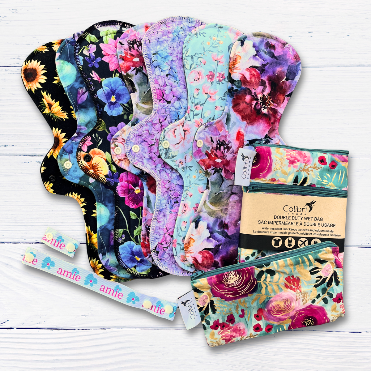 Set of floral-patterned reusable pads with two wet bags a drying strap and a wing extender on a white wooden surface