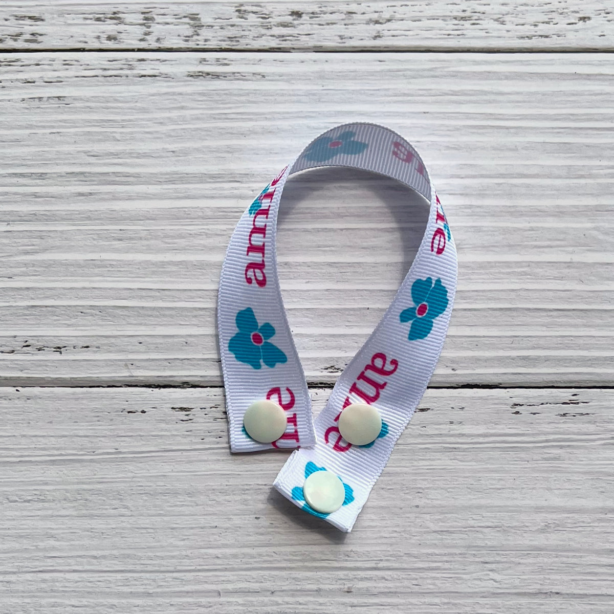 reusable pad drying strap with ribbon printed with the amie logo and three snaps laid in a crescent shape on a rustic white wood background