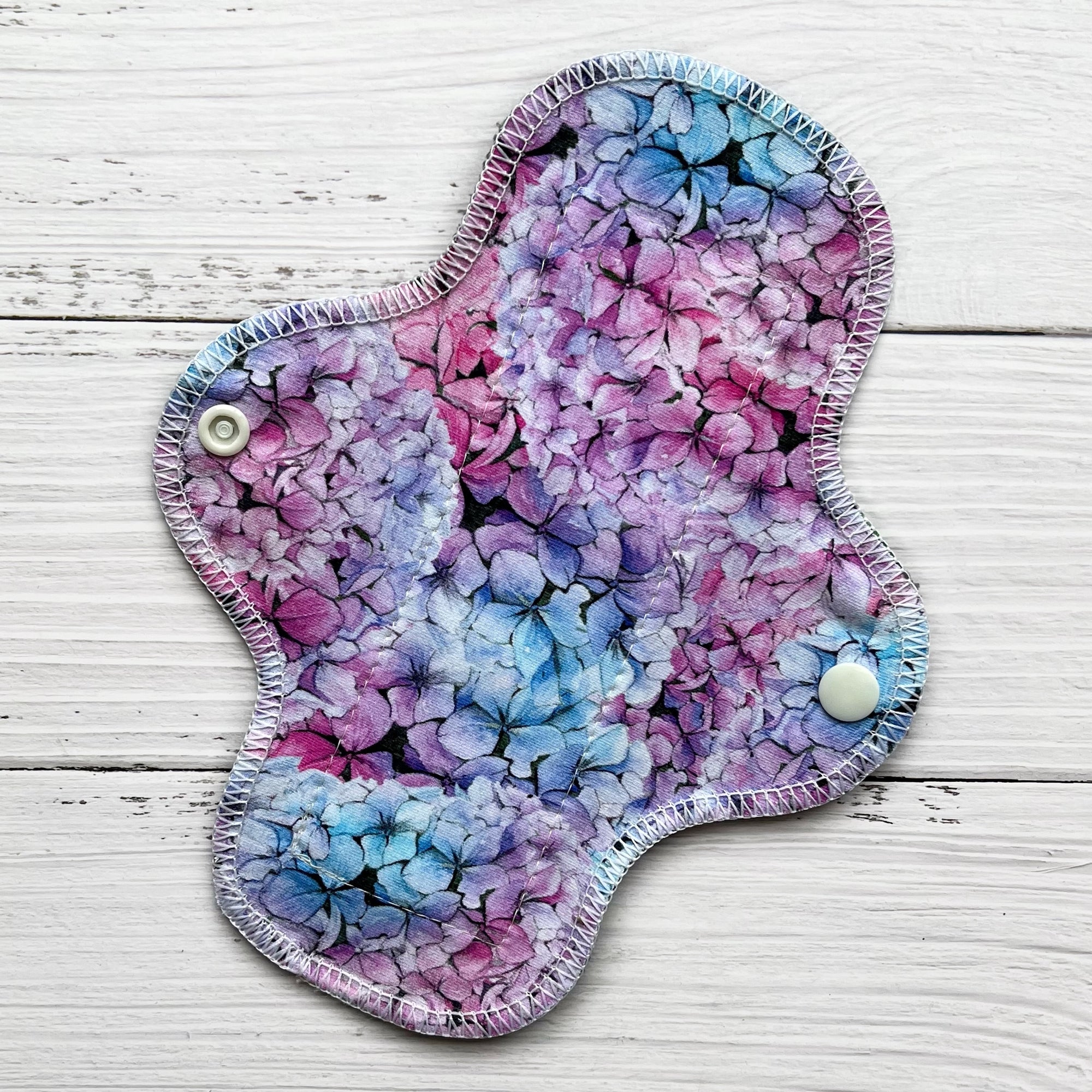 reusable pad in a pink blue and purple hydrangea print on a rustic wood background