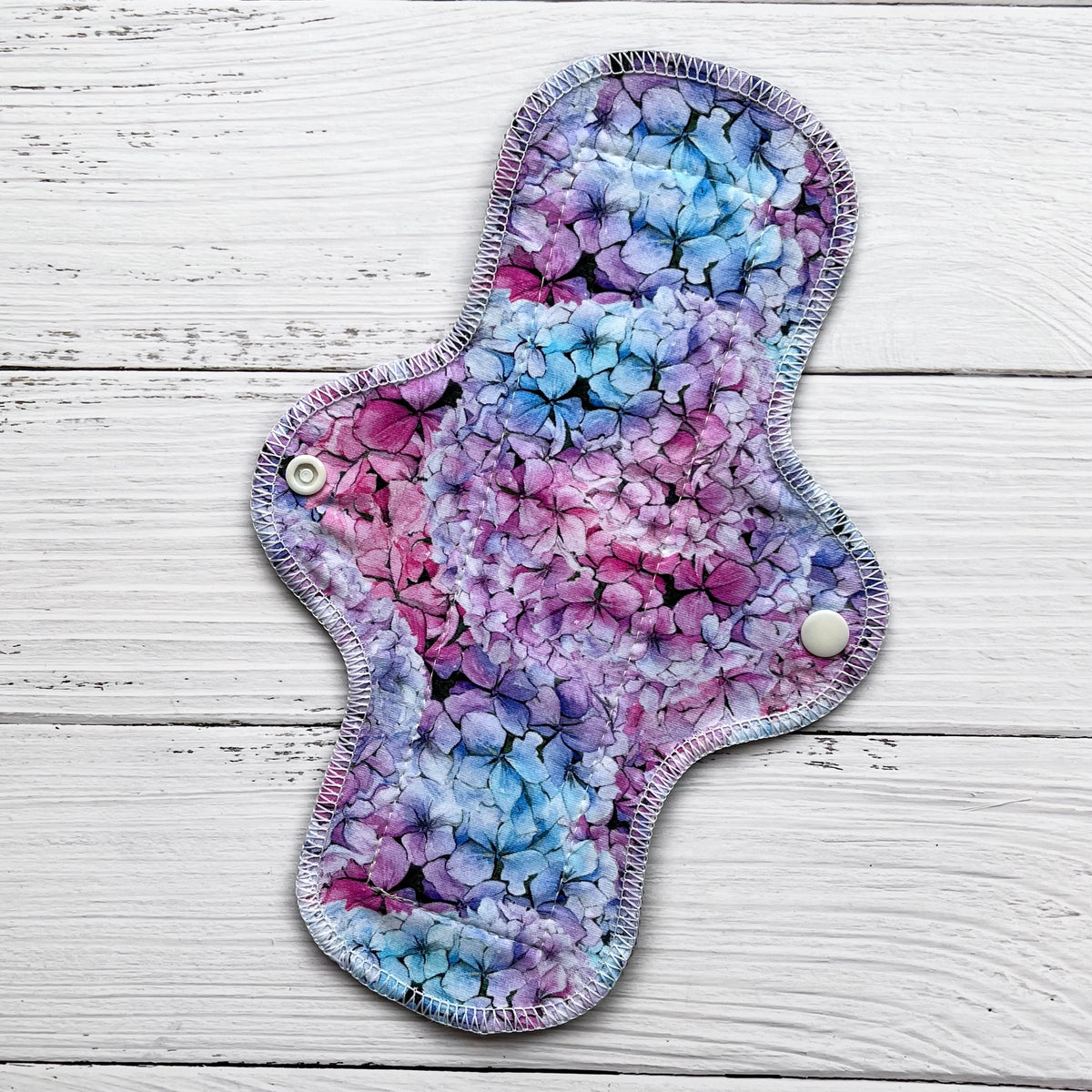 10 inch long reusable pad with a blue pink and purple hydrangea print on a rustic wood background
