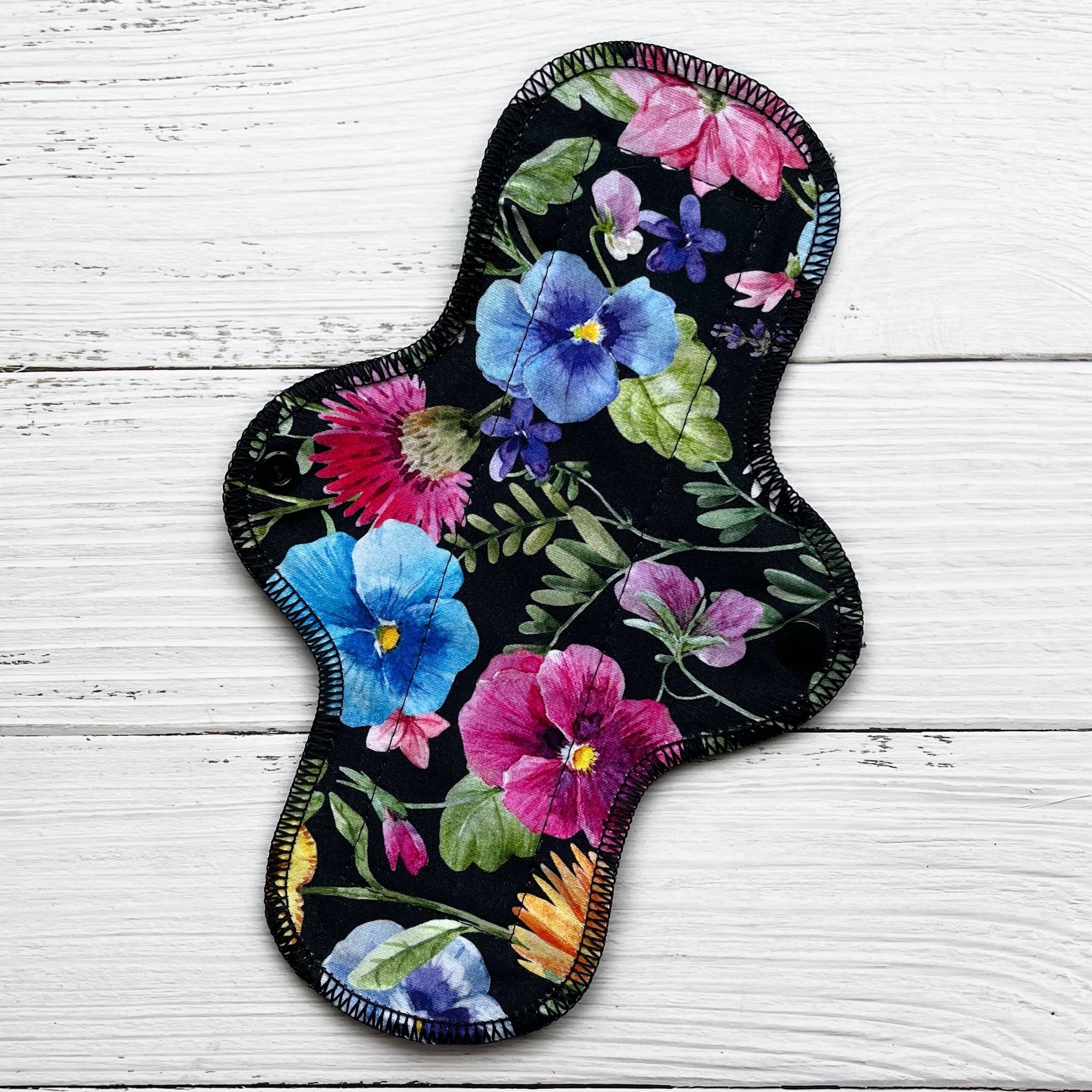 10 inch long reusable pad with a bold pansy on black print on a rustic wood background
