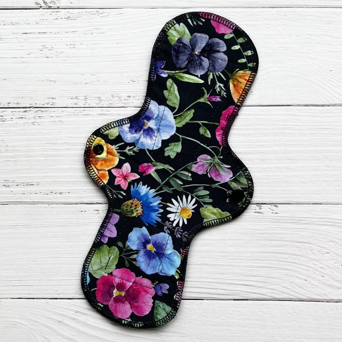 12 inch long reusable pad with a bold pansy on black print on a rustic wood background