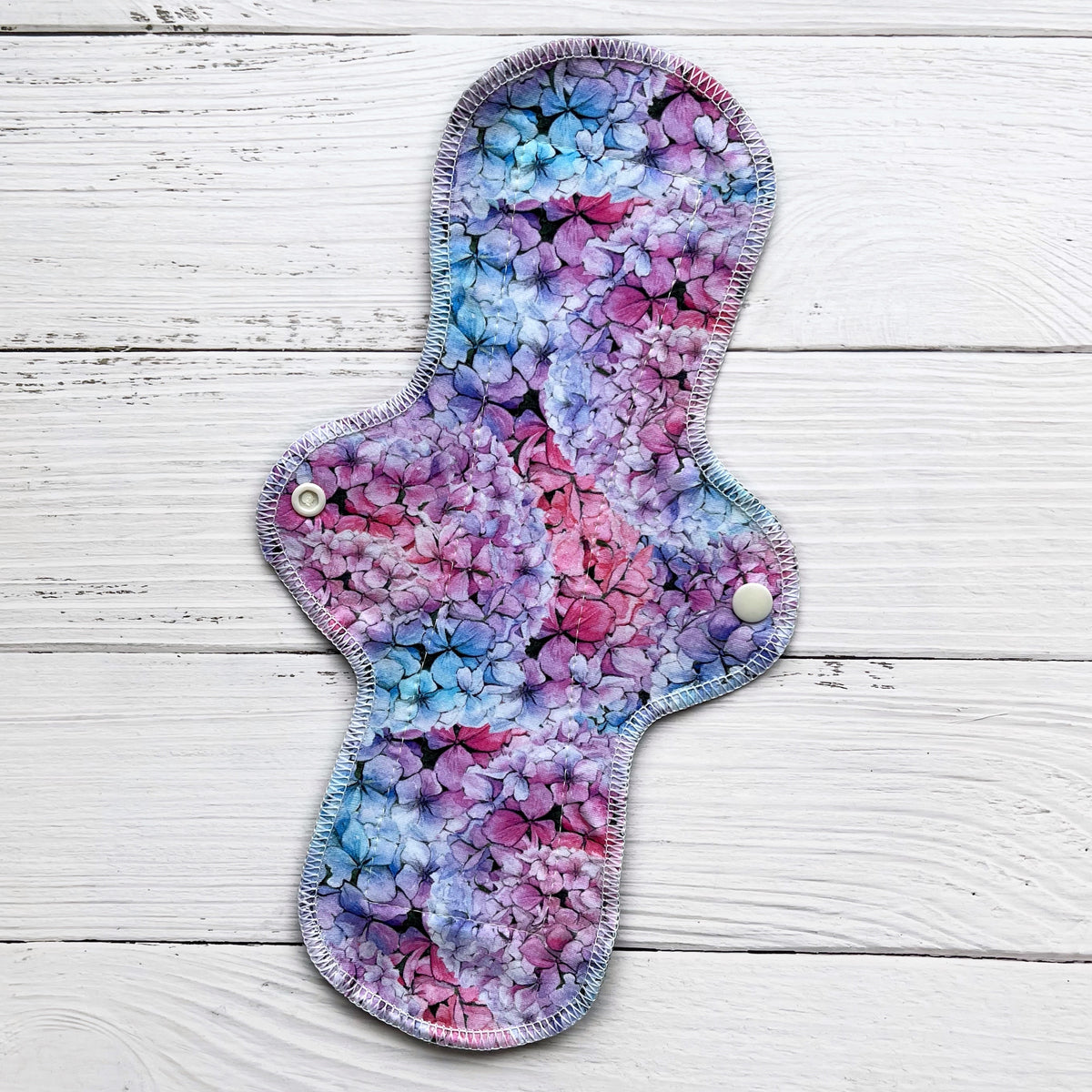 12 inch long reusable pad with a blue pink and purple hydrangea print on a rustic wood background