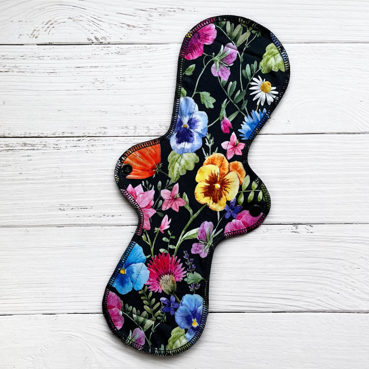 14 inch reusable pad with a bold pansy on black print on a rustic wood background