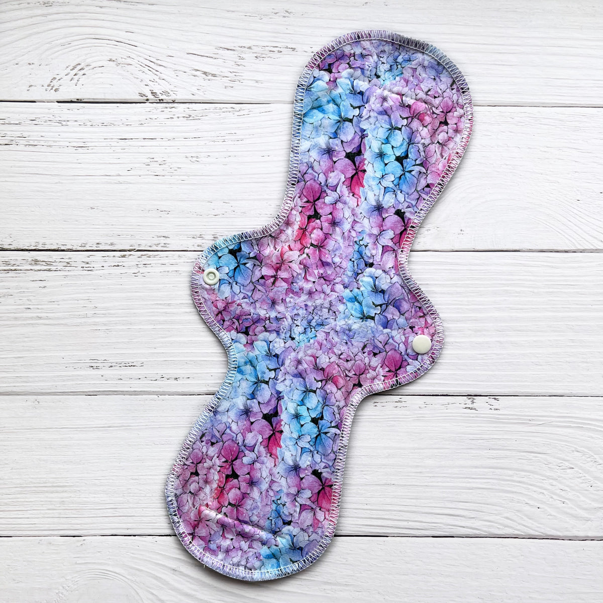 14 inch long reusable pad with a blue pink and purple hydrangea print on a rustic wood background