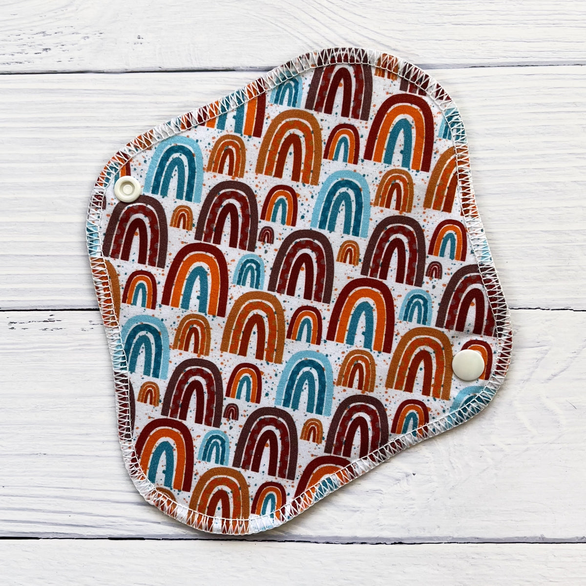 reusable liner in a neutral rainbow print on a rustic wood background