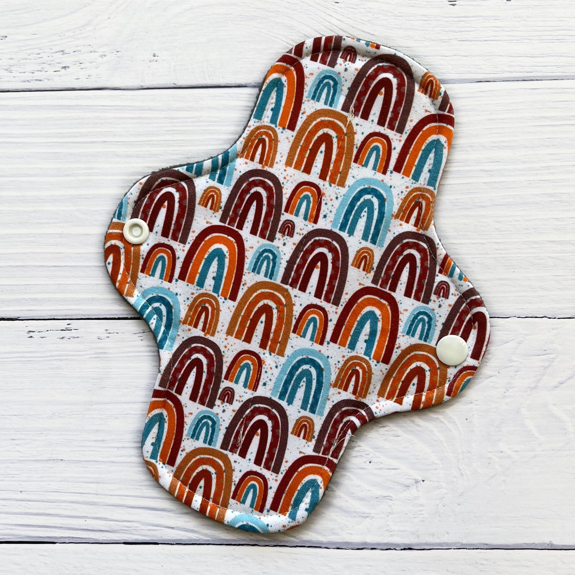 short reusable pad in a neutral rainbow print on a rustic wood background