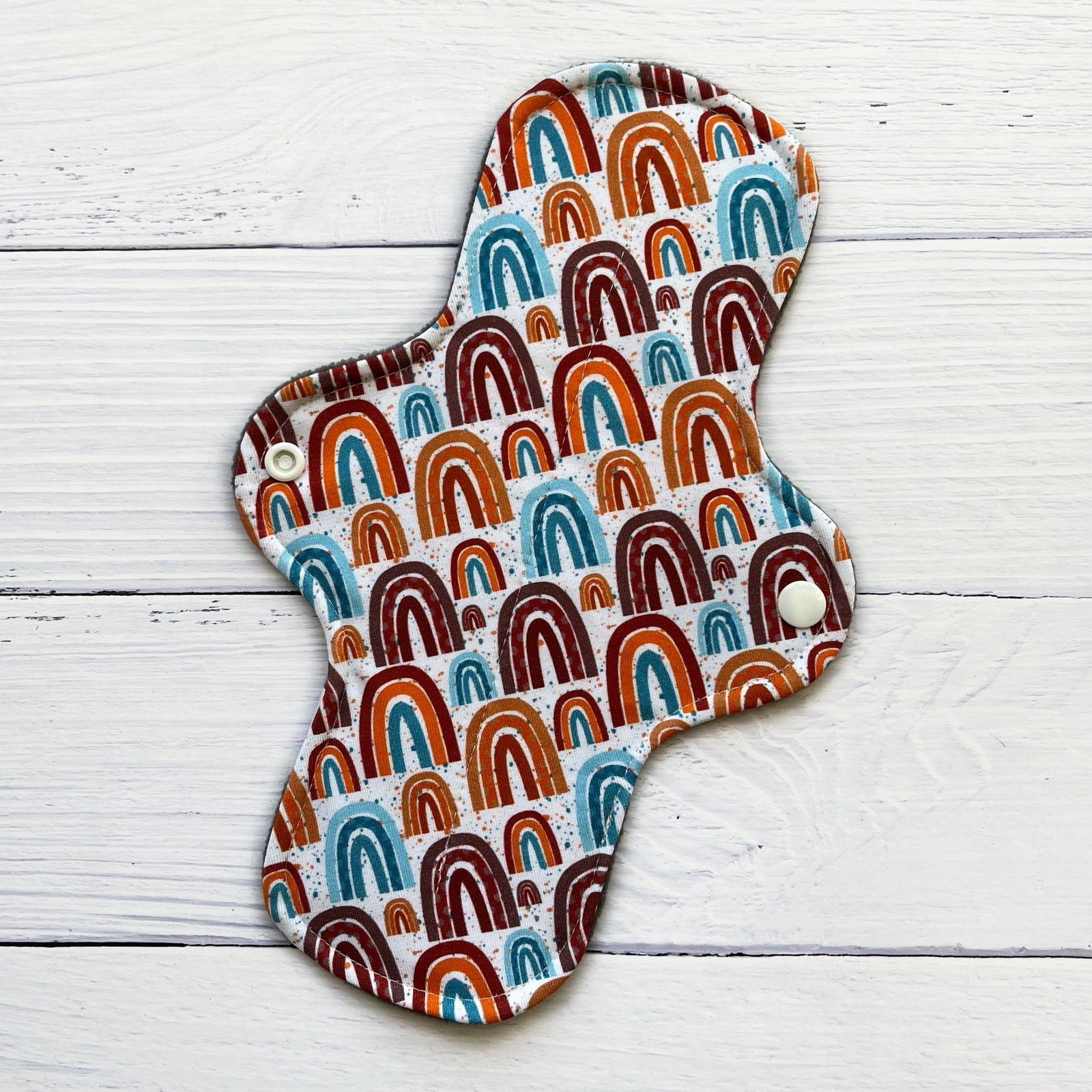 reusable pad in a neutral rainbow print on a rustic wood background