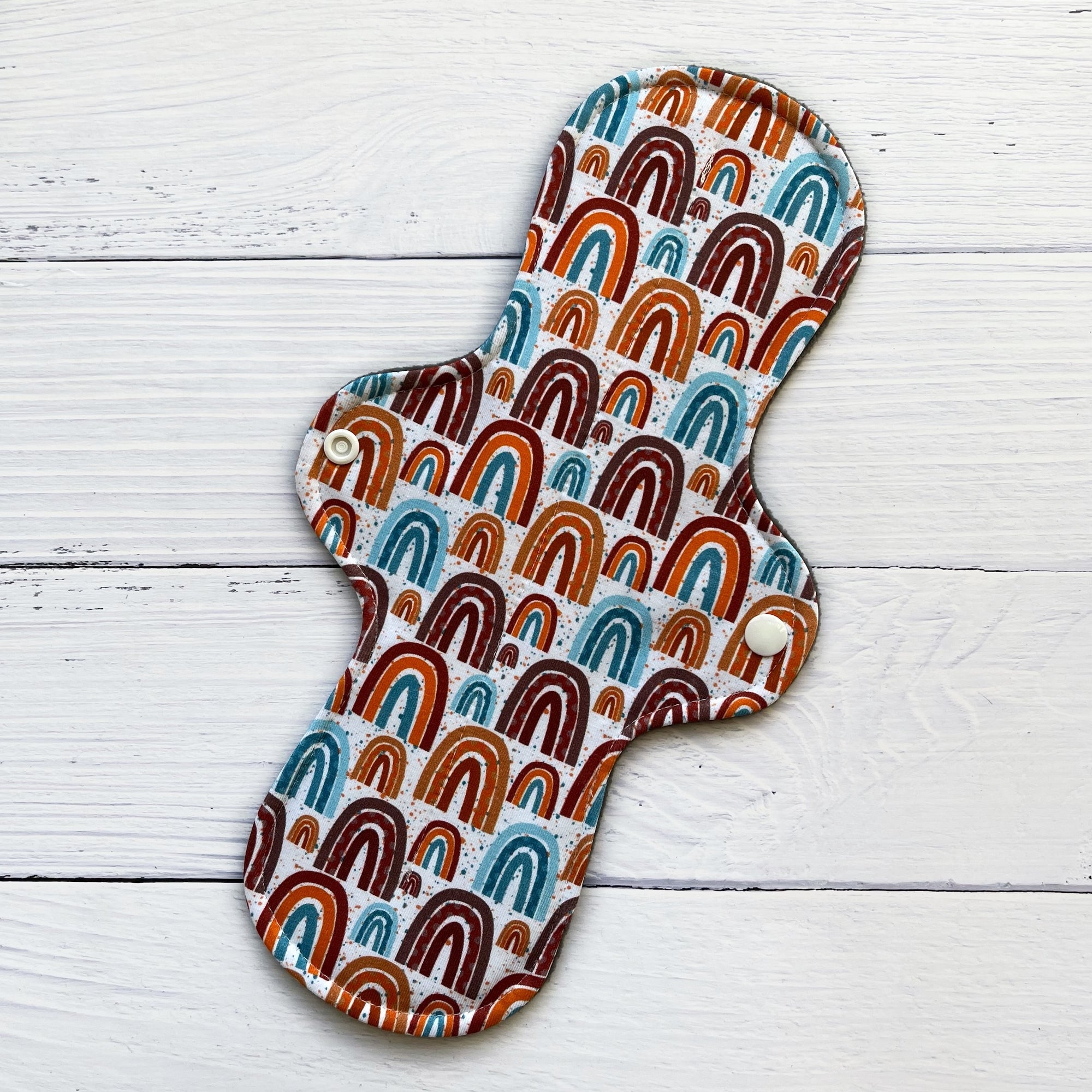 long reusable pad in a neutral rainbow print on a rustic wood background