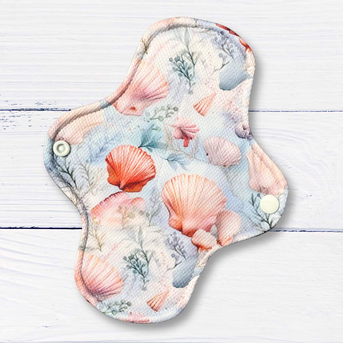 Reusable menstrual pad with seashell pattern on a wooden surface
