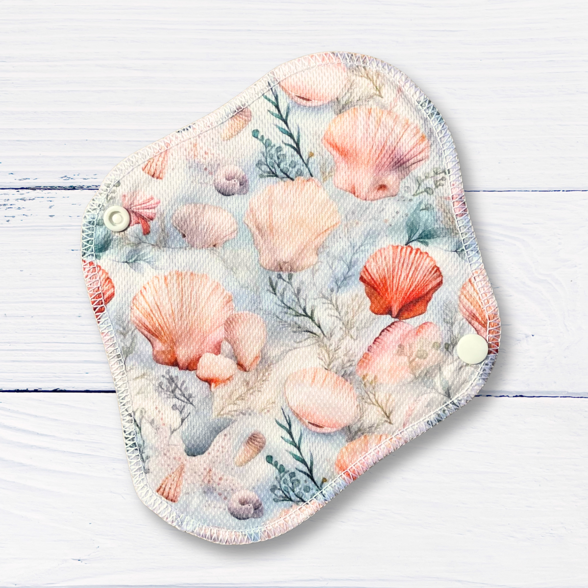 Reusable menstrual pad with seashell pattern on a wooden surface