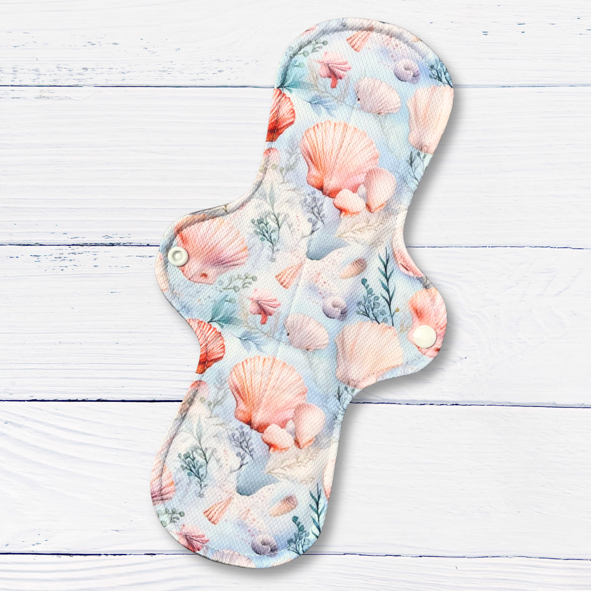 Reusable menstrual pad with seashell pattern on a wooden surface