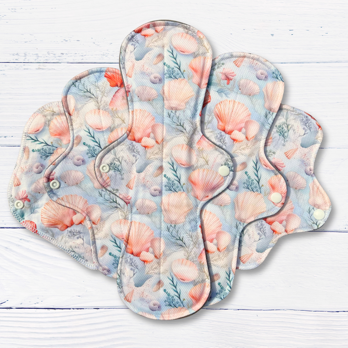 set of 5 seashell print reusable sanitary pads on a white wood surface
