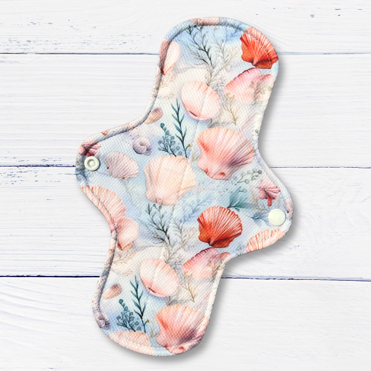 Reusable menstrual pad with seashell pattern on a wooden surface