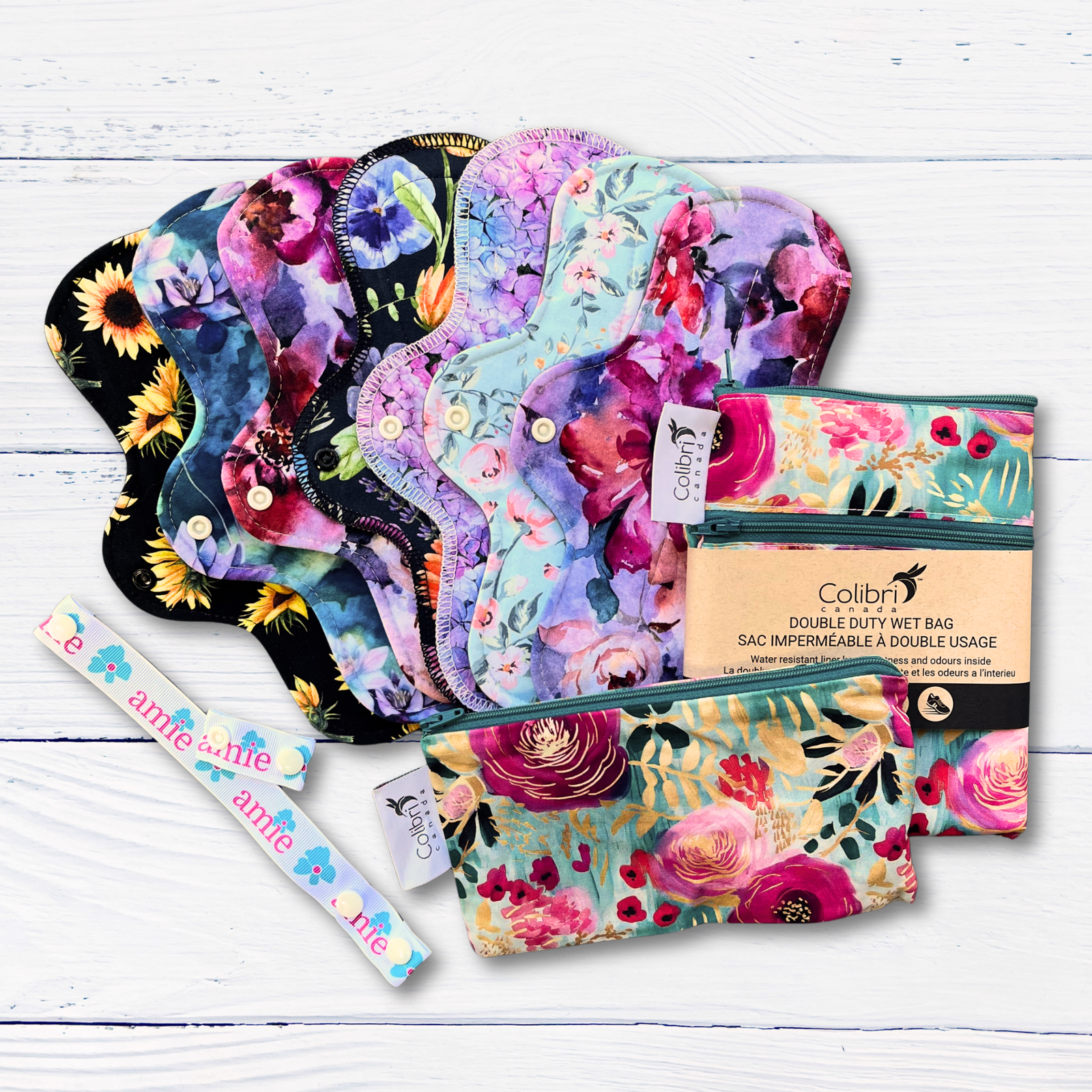 Colorful floral-patterned standard length pads with two Colibri double-duty wet bags on a white wooden surface.