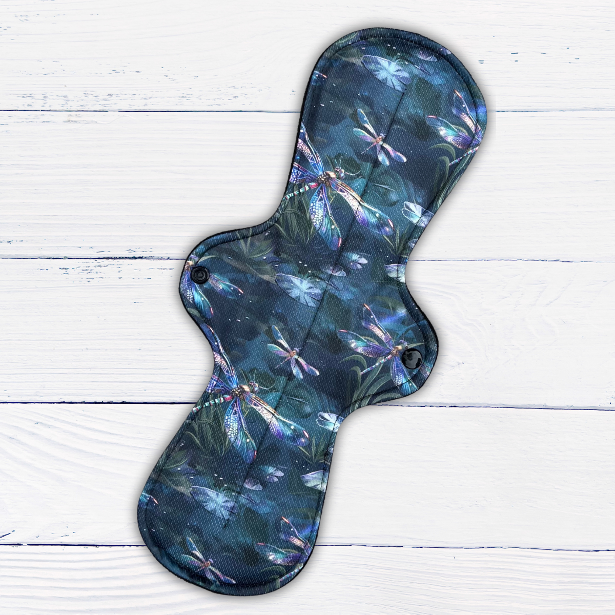 extra-long heavy absorbency reusable pad in a dragonfly print athletic wicking jersey on a rustic white wood background