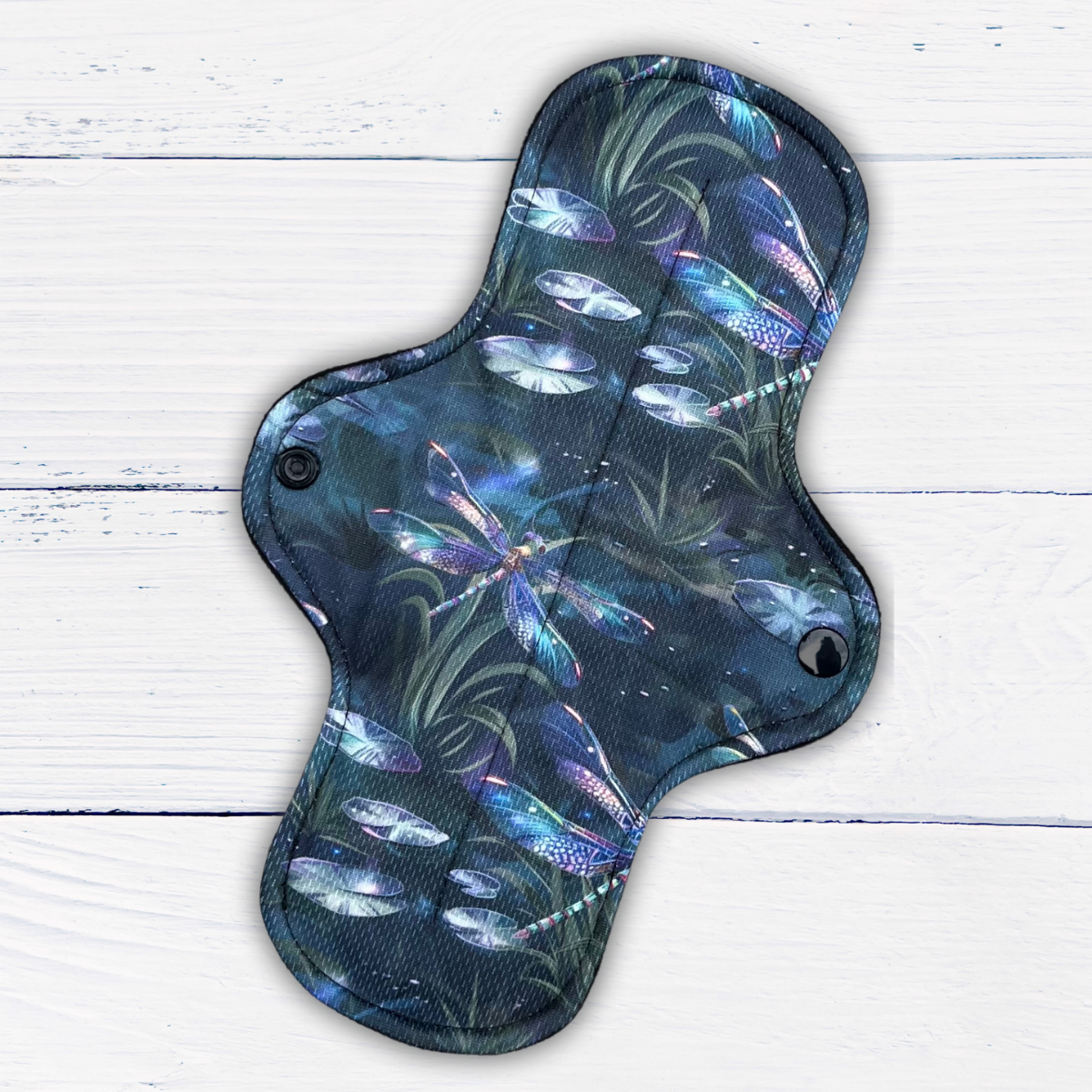 moderate absorbency reusable pad in a dragonfly print athletic wicking jersey on a rustic white wood background