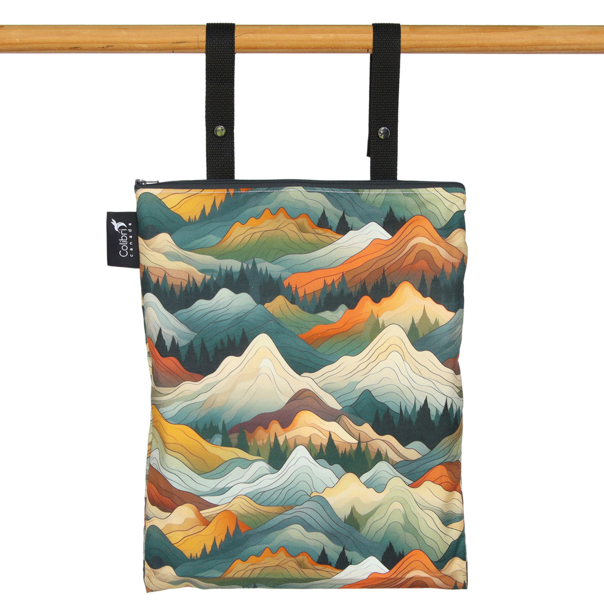 A waterproof zippered tote bag with a colourful mountain landscape print, hanging from black straps on a wooden rod against a white background.