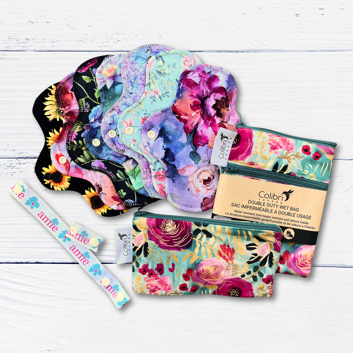 Floral-patterned standard short reusable pads with two Colibri branded wet bags on a white wooden surface
