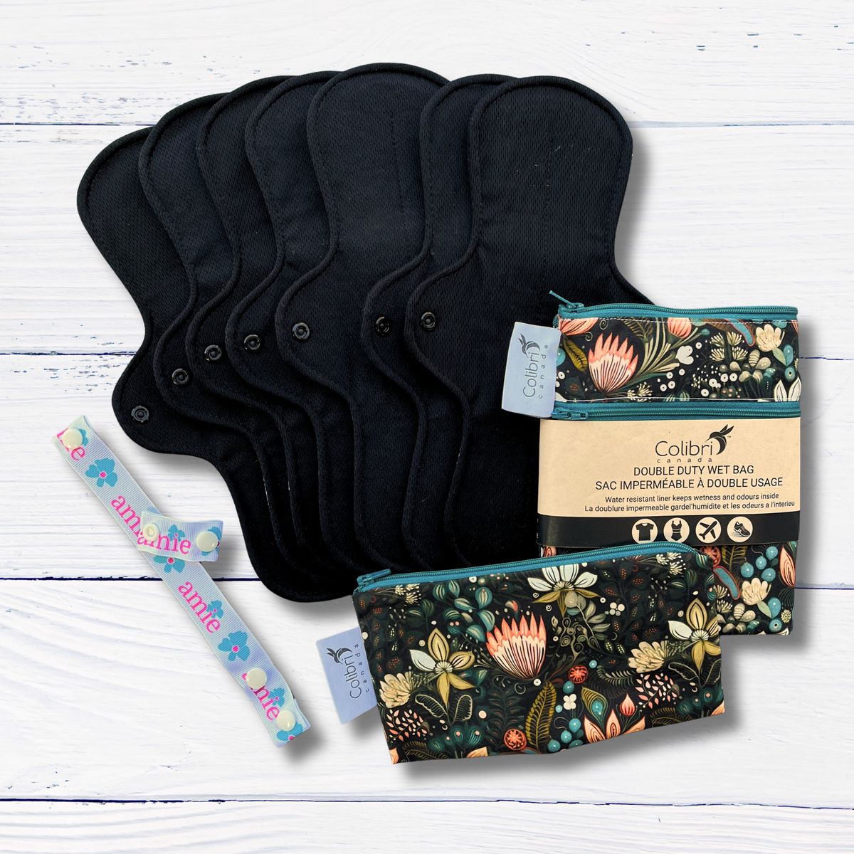 Set of black cloth pads with floral-patterned wet bags on a white wooden surface