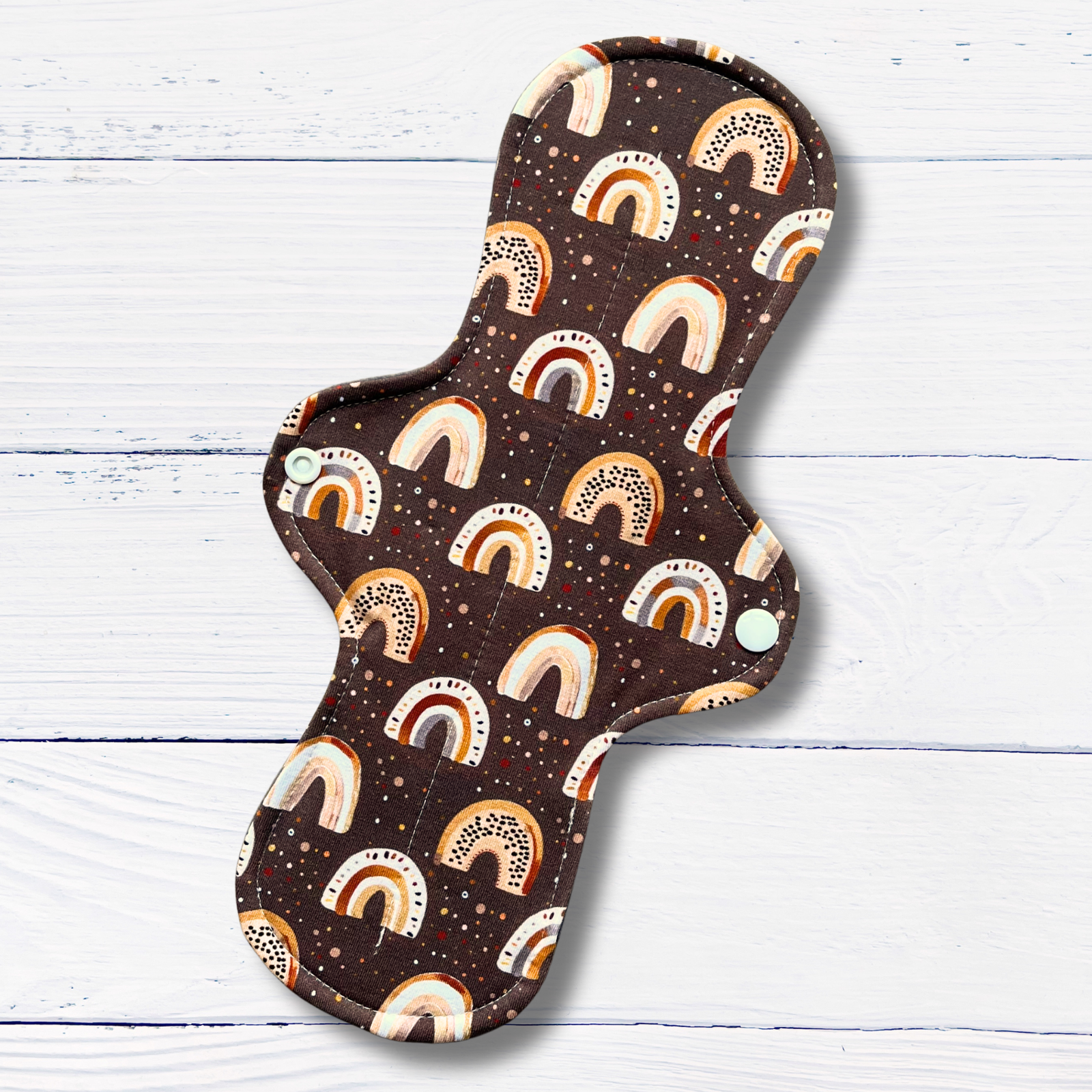 reusable menstrual or incontinence pad with rainbow pattern on a wooden surface
