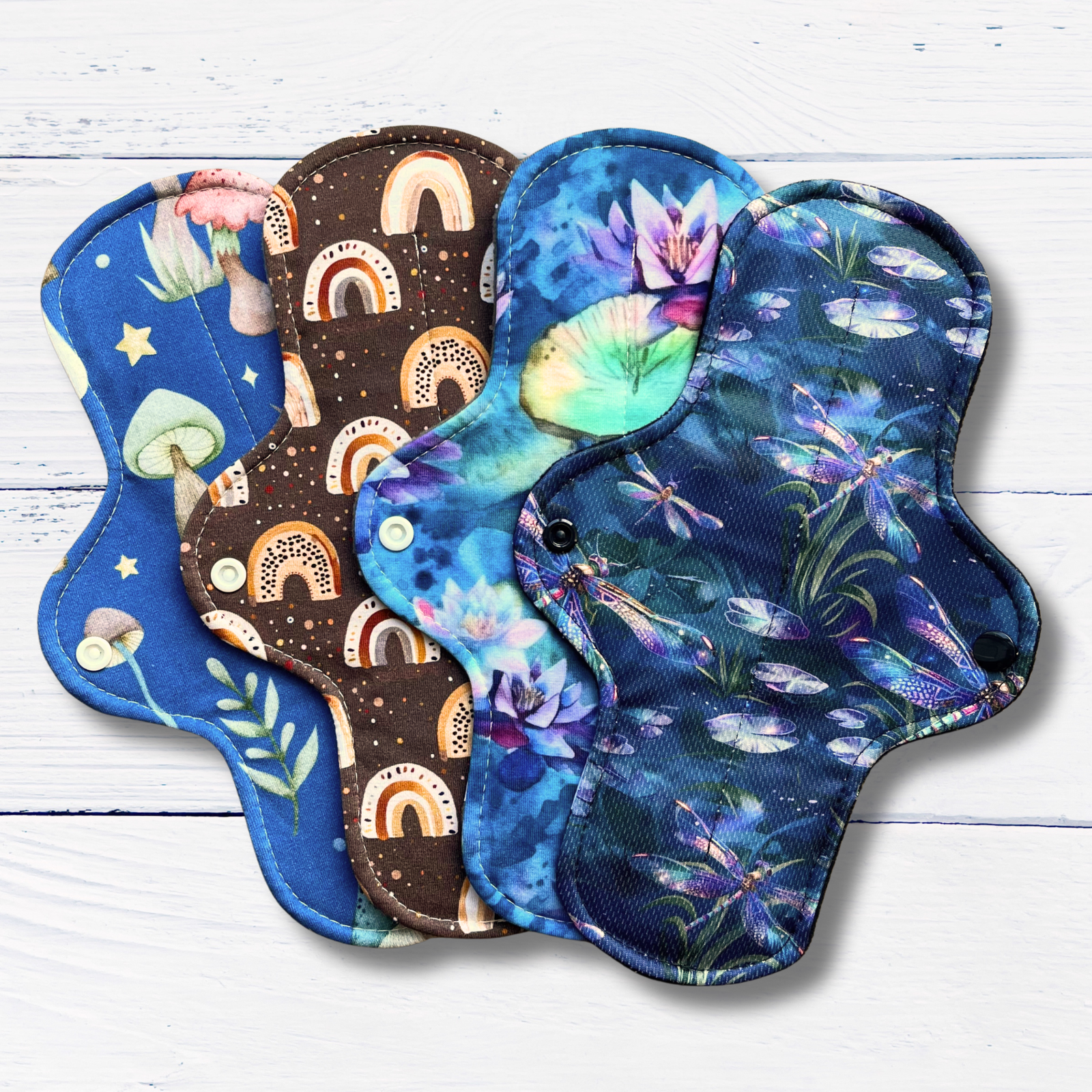 Set of four colourful reusable pads with nature-themed designs on a white wooden surface