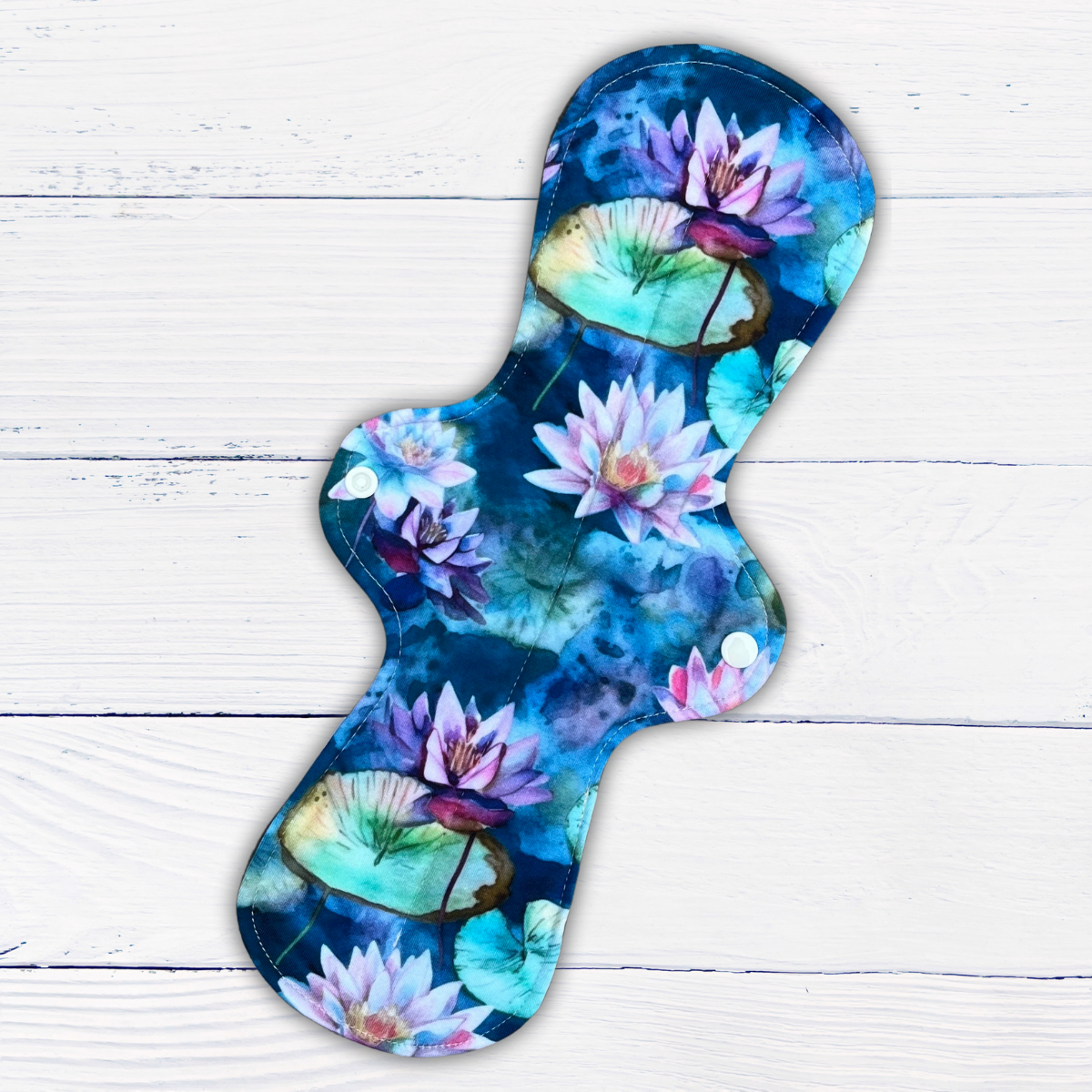 extra long heavy absorbency reusable pad in a water lily print in shades of green, blue and purple on a rustic wood background
