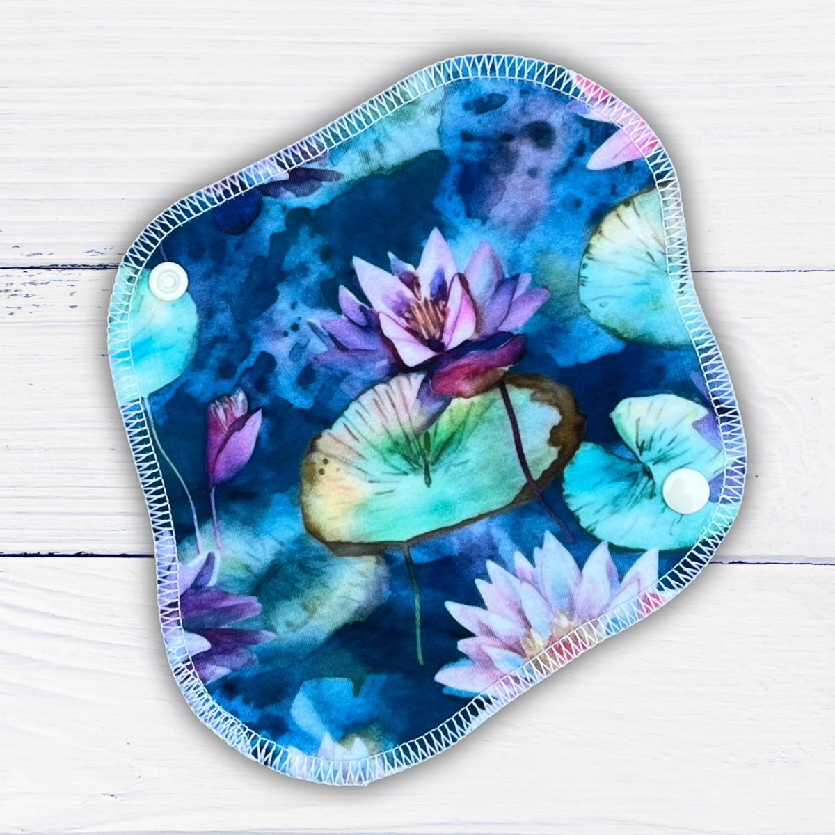 reusable panty liner in a water lily print in shades of blue, green and purple on a rustic white wood background