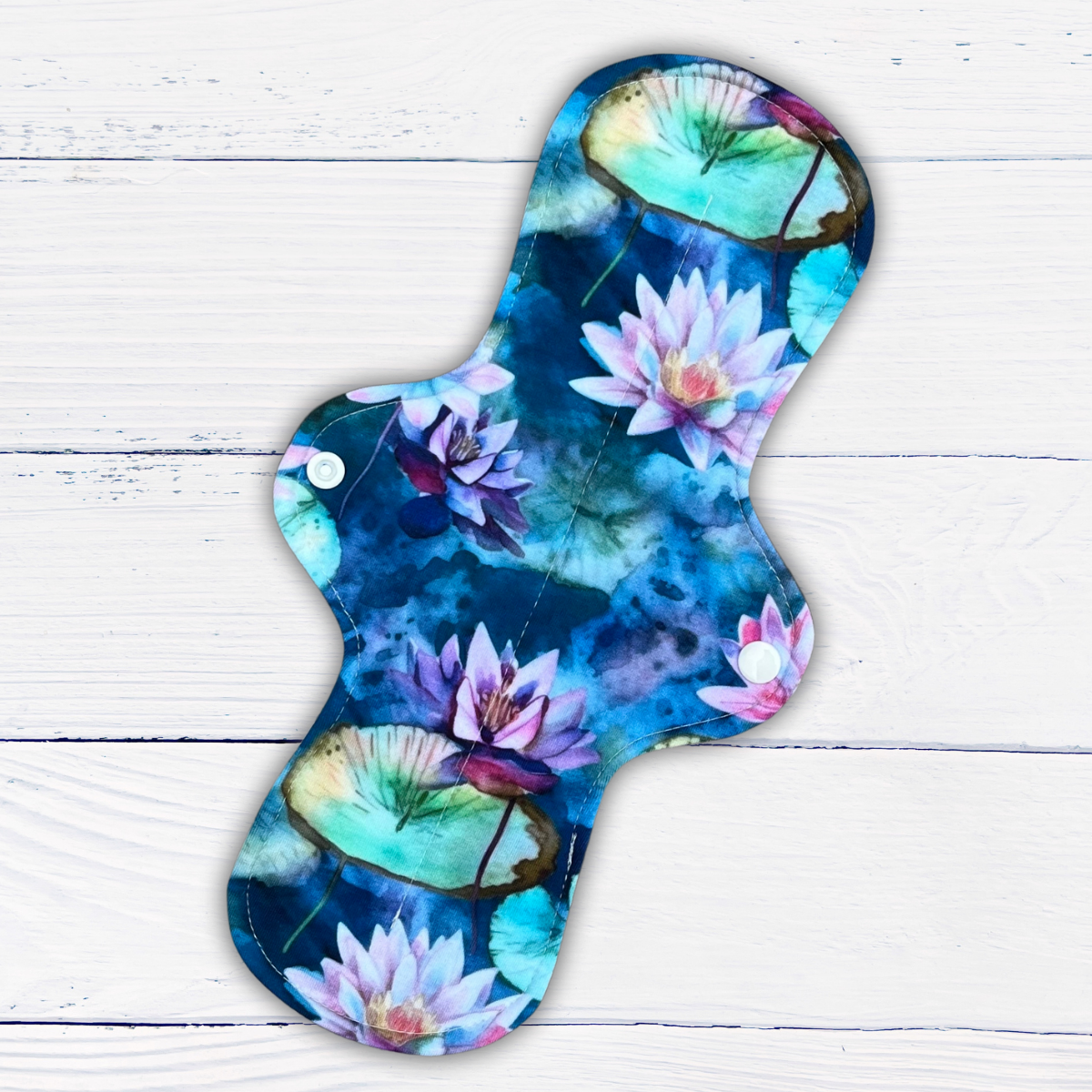 long reusable pad in a water lily print in shades of blue green and purple on a rustic white wood background