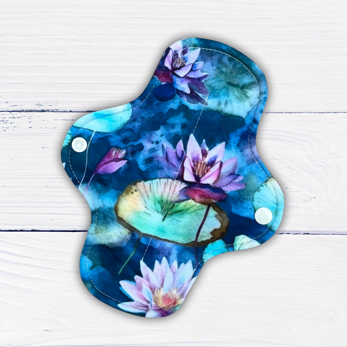 light absorbency reusable pad in a water lily print in shades of blue green and purple on a rustic white wood background