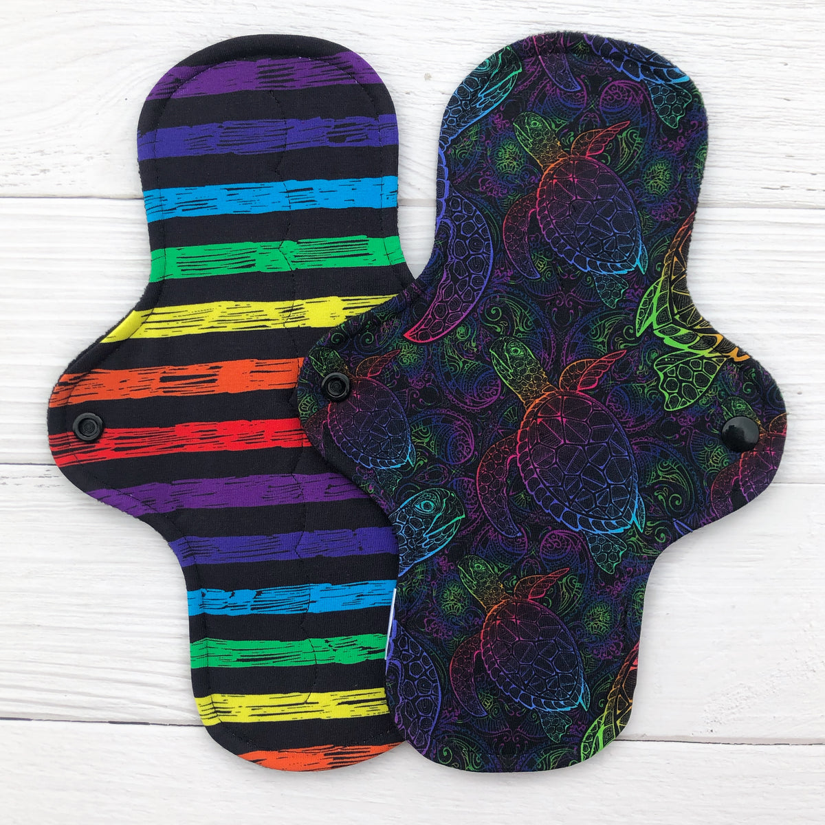 two reusable pads in rainbow on black print with rainbow stripes and rainbow turtles