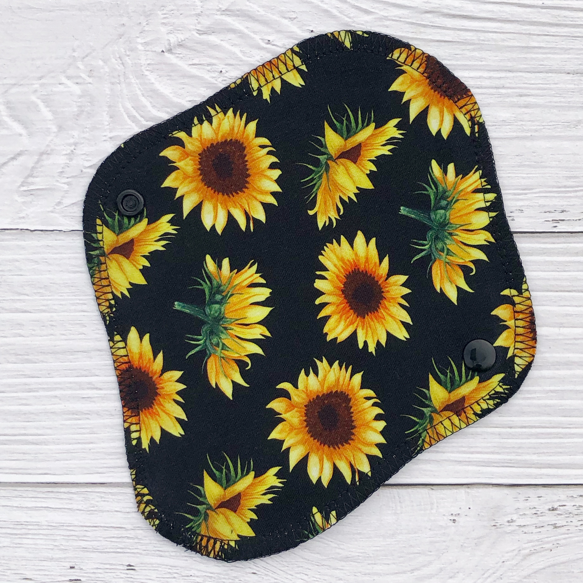 sunflowers on black print reusable pantyliner on faux white wood background