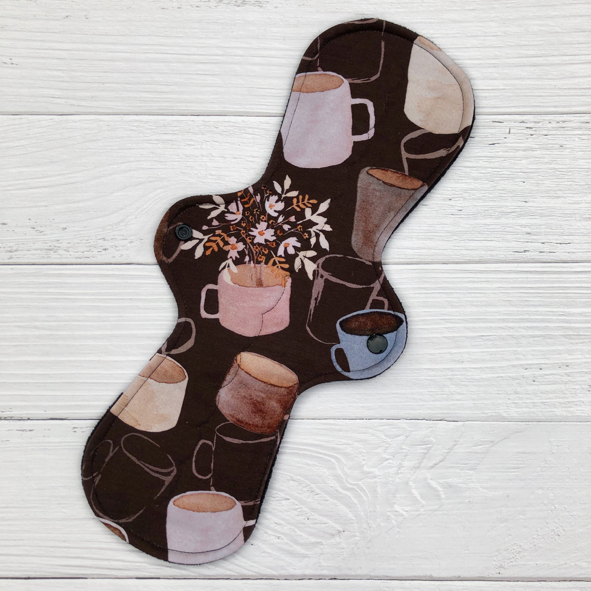 reusable pad in a coffee cup and floral print on a white wood background