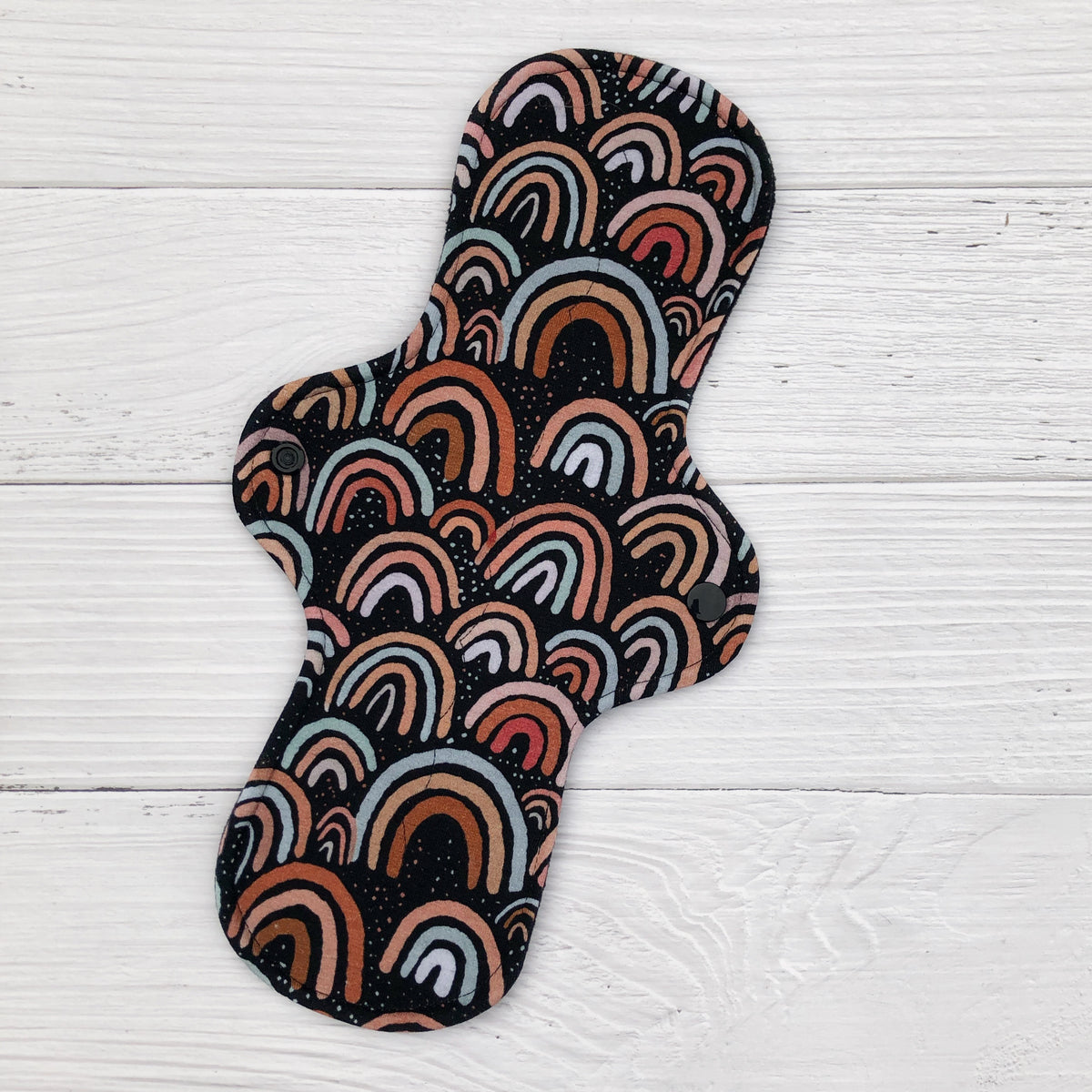 reusable pad in a neutral rainbow on dark brown print on a white wood background