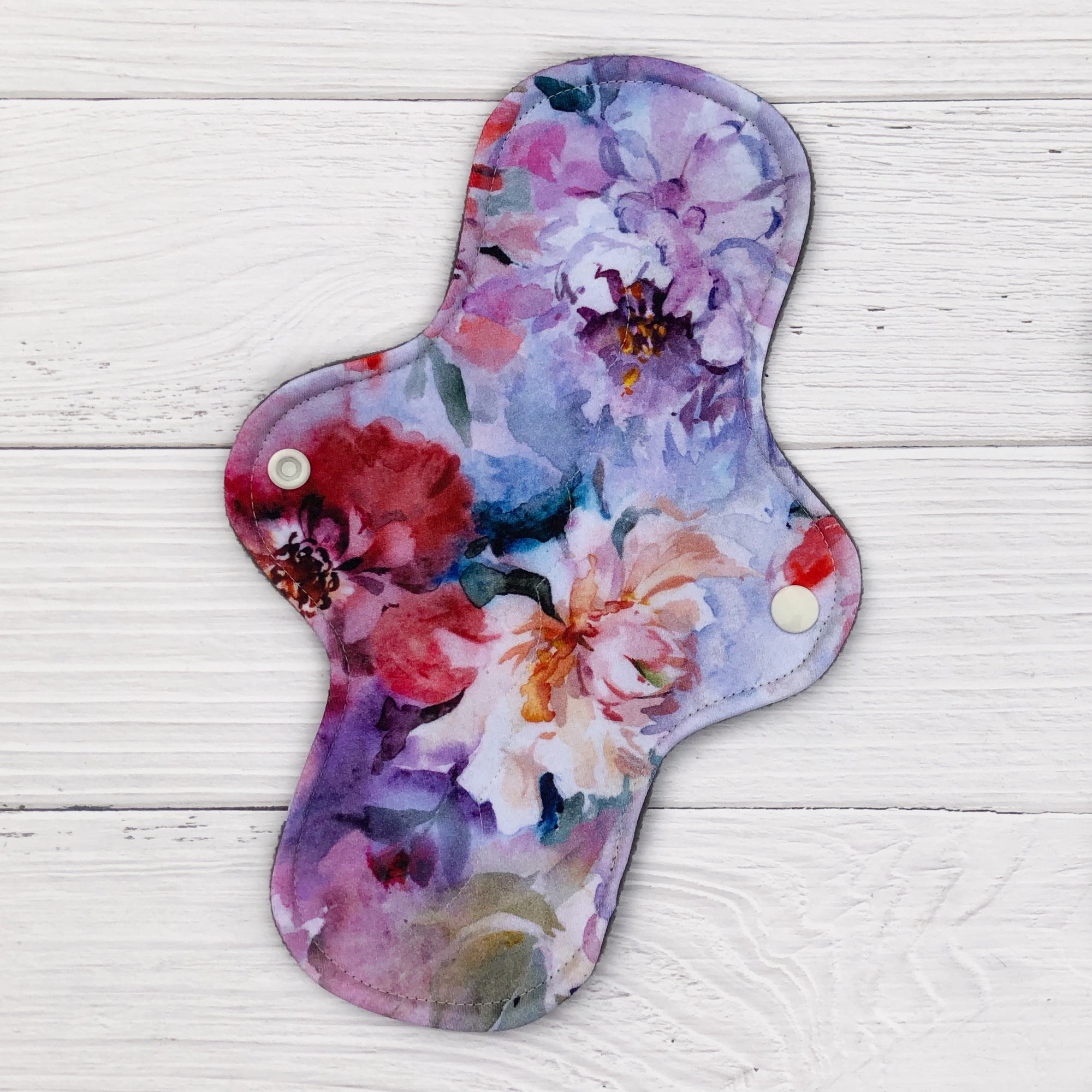 reusable pad in a watercolour peony print on a white wood background