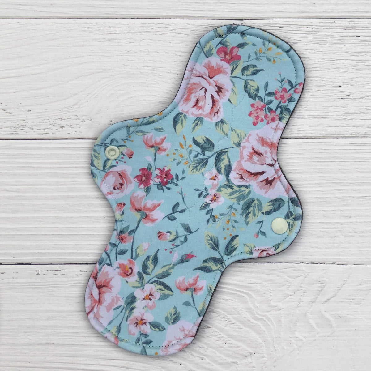 reusable pad in a mint floral print on a white wood background