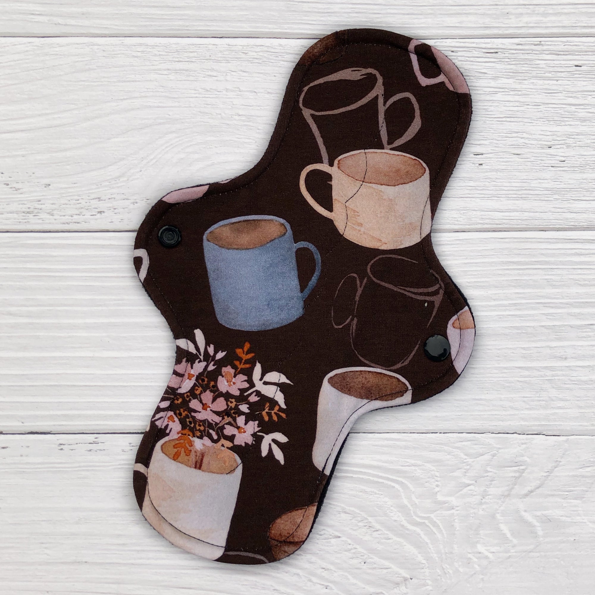 reusable pad in a coffee and floral print on a white wood background