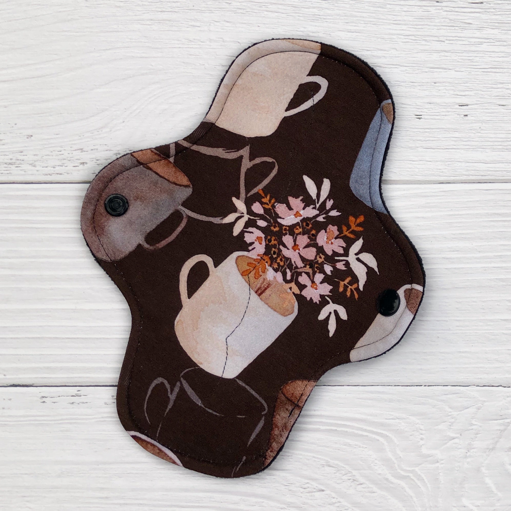 reusable pad in a coffee and floral on brown print on a white wood background