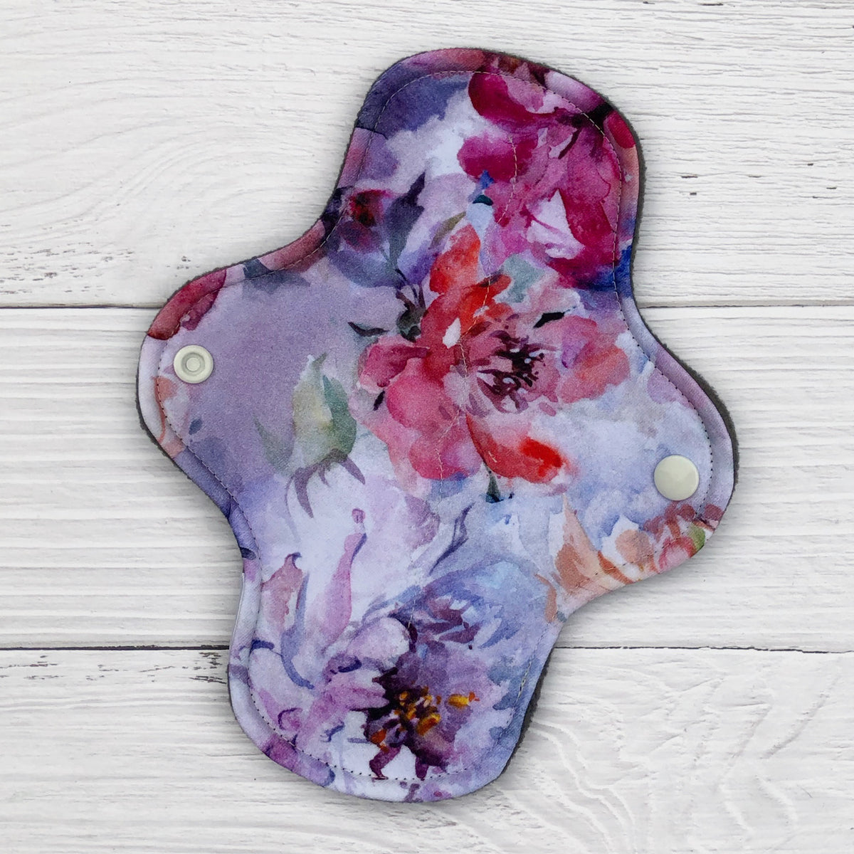 reusable pad in a peony watercolour print on a white wood background