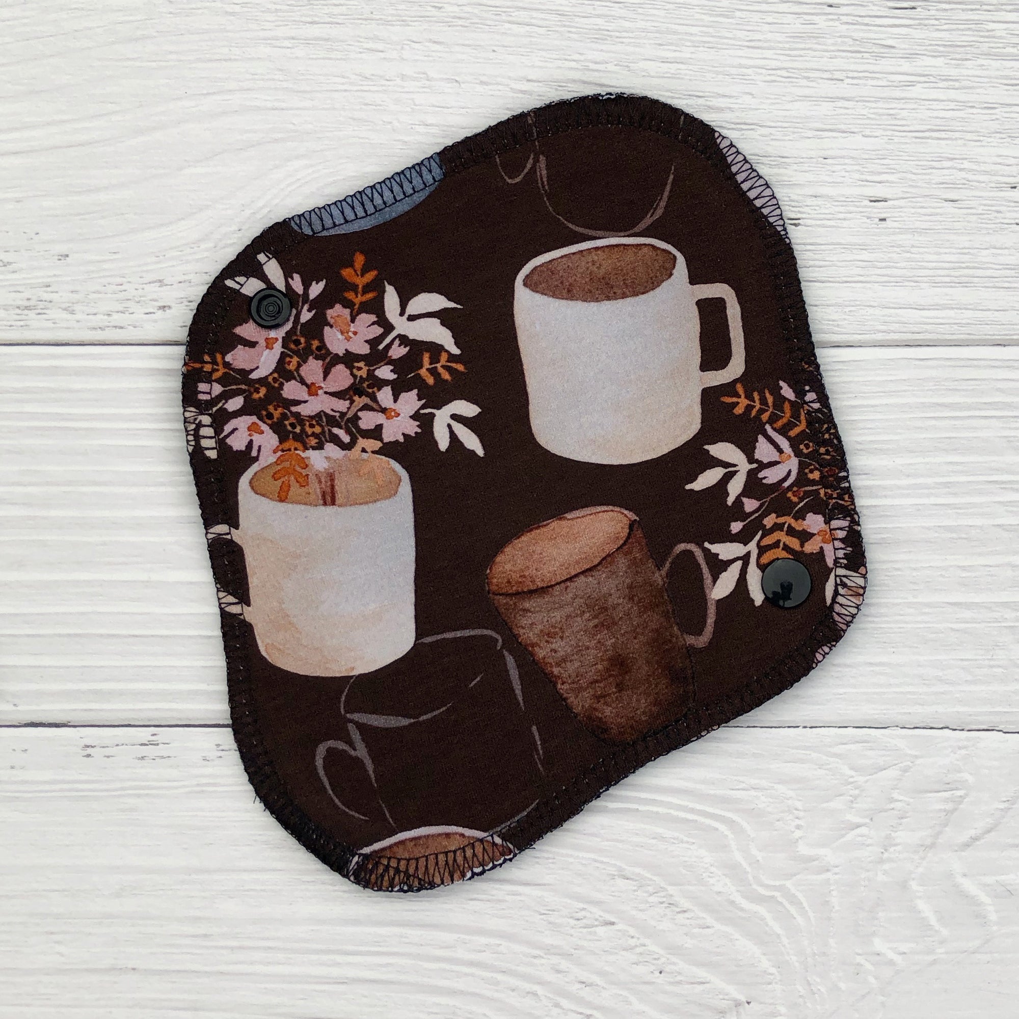 reusable pantyliner in a coffee and floral print on a white wood background