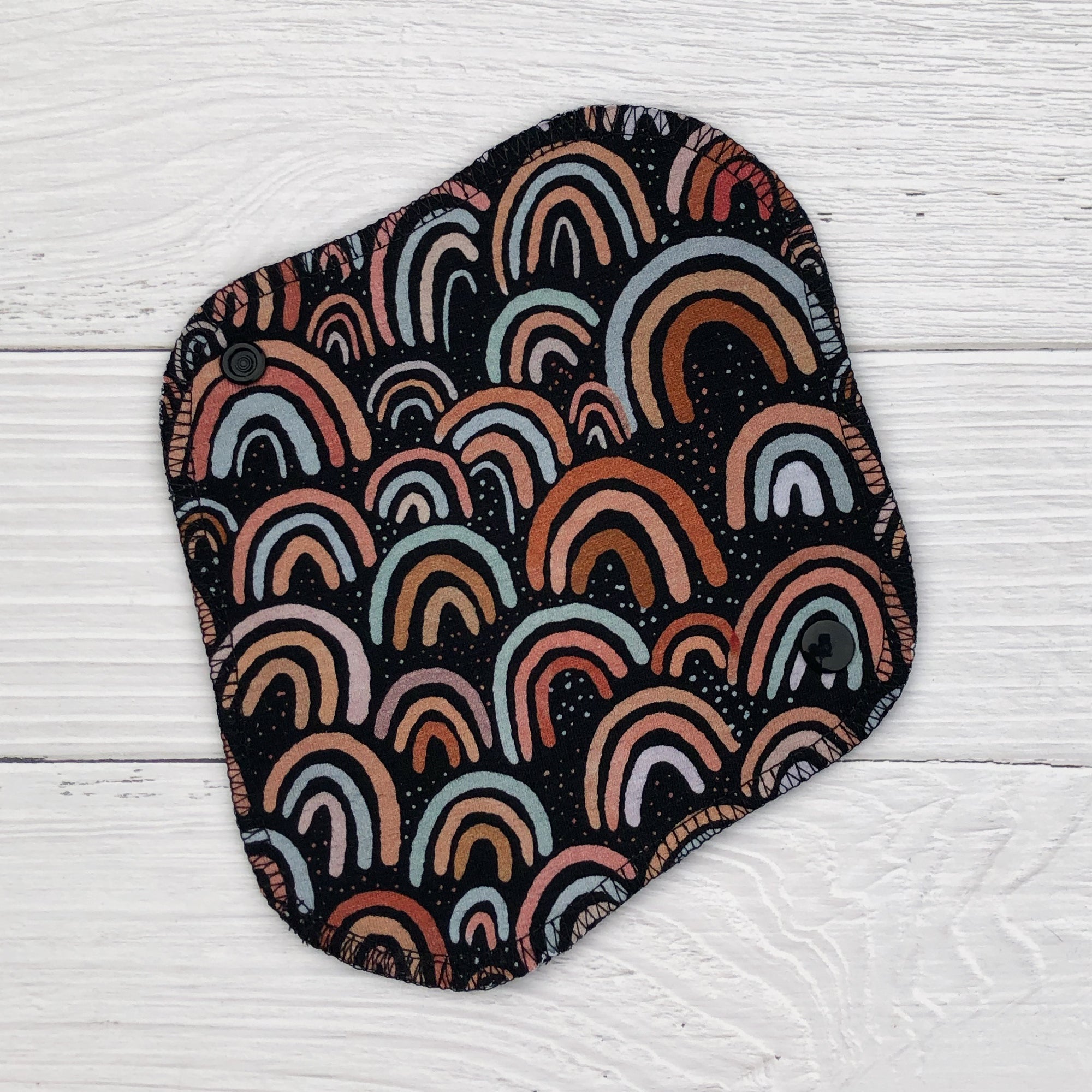 reusable pantyliner in a neutral rainbow print on a white wood background